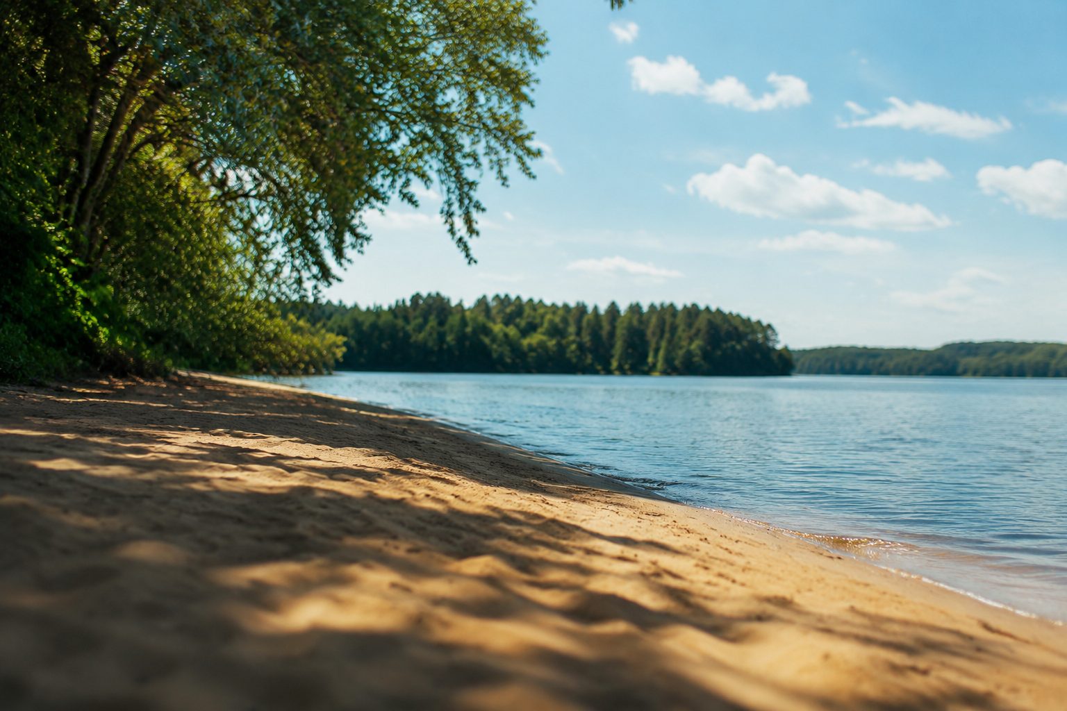 Plaża nad mazurskim jeziorem, ciepły piasek, drzewa rzucają cień